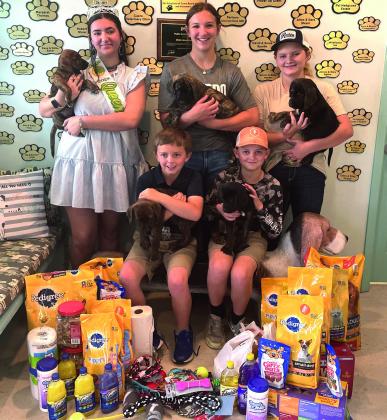 Five members of the DeWitt County 4H Club donate a collection of pet and shelter supplies. Representing the group (L to R, standing) 4H Queen Kassidy Cowey, Ella Jander and Kaitlyn Roeder. Seated (L to R) with more pups on the famous “weiner dog” bench is Eli Roeder and Carter Roeder.